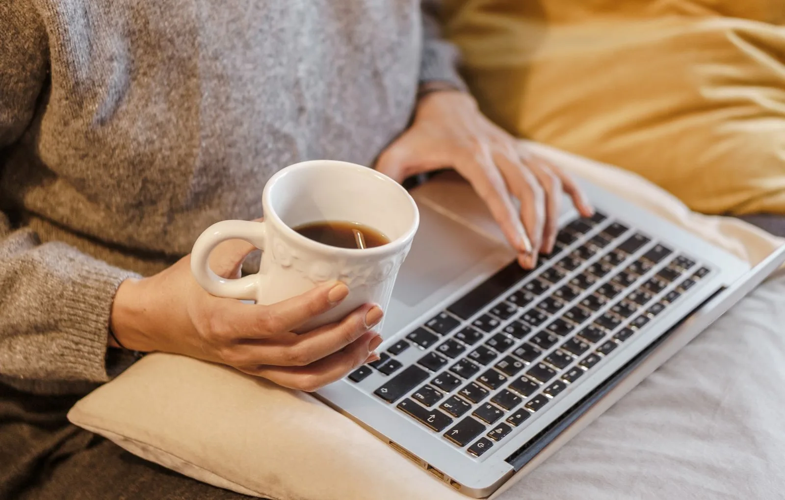 Osoba pracująca na laptopie z filiżanką kawy